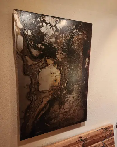 Large abstract poured panel in bronze, copper and cream hung on a stucco wall, above a live edge shelf with blue filled fractal burns