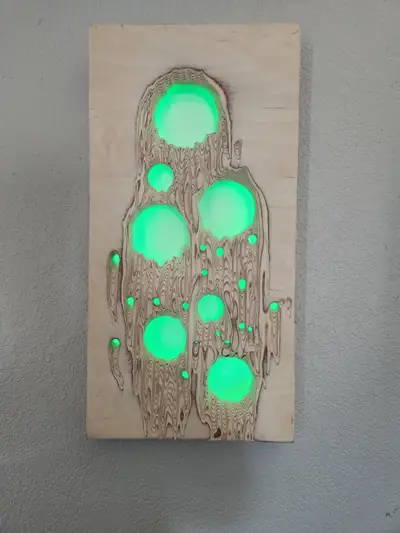 A carved wood wall panel with round openings filled with resin, lit from behind in green.