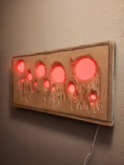 A long wood wall panel set with round red resin discs lit from behind, mounted on a plain wall.