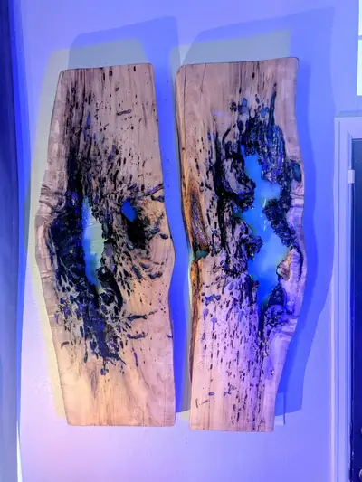 Two live edge wood wall panels lit from behind with blue light, showing the epoxy filled voids as silhouette