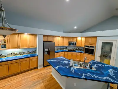 A full kitchen in deep blue and white ocean epoxy, counters and island poured to look like breaking surf against oak cabinets.