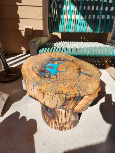A round burl stump side table with turquoise epoxy filling its natural voids, on a live edge trunk base.