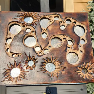 The same carved cell and starburst panel outdoors in daylight, showing the scorched grain around each opening and the brushed metallic finish inside them