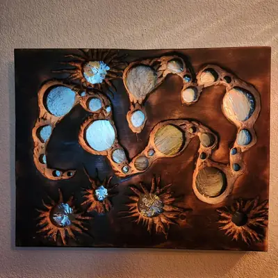 Carved wood wall panel in a scorched dark finish, with linked cell shapes and starbursts opened through to a pale brushed surface, hung on a stucco wall