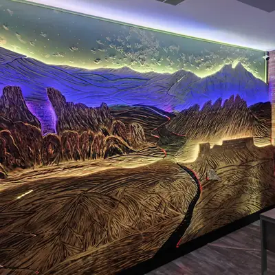 A wall length carved mountain mural washed in purple and gold backlighting, spanning a whole room.