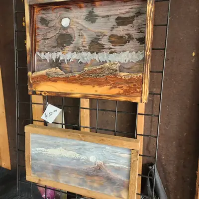 Two carved mountain scene wood panels displayed on a rack in the workshop