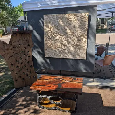 Carved wood panels and a live edge piece displayed at an outdoor art show