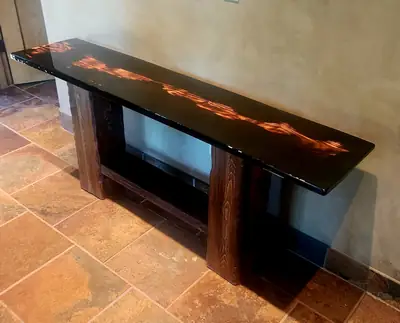 A dark console table with a molten orange epoxy vein running the length of its top, standing against a warm wall.