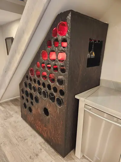 A bar built into a stairwell, its dark textured front set with rows of round red resin discs lit from behind.