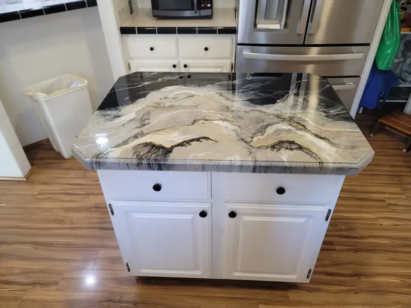 Kitchen island with an epoxy countertop poured to a black and white marble effect on white cabinets