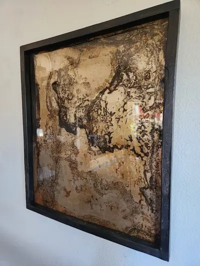 Framed abstract epoxy wall art in gold and grey, photographed at an angle on a white wall
