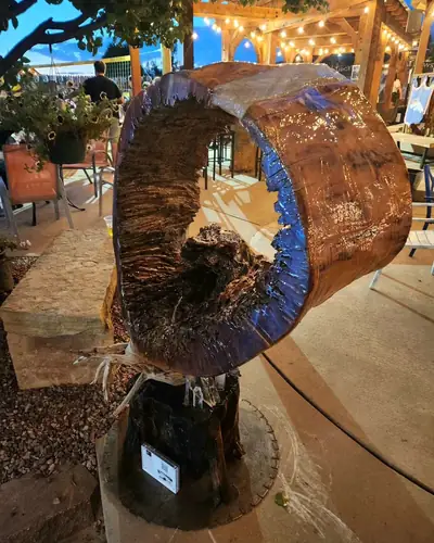 Hollow log section finished with blue and purple resin and mounted on a stump base, displayed on an outdoor patio under string lights at dusk