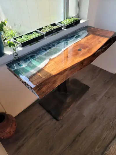 A live edge wood bar counter mounted at window height, with a glass panel below and a planter box running its length.
