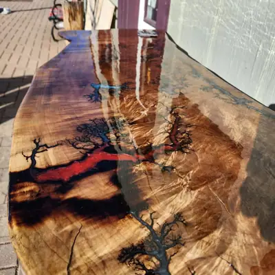 Long glossy live edge bar top with fractal burns filled in black, blue and red resin, photographed outdoors in direct sun