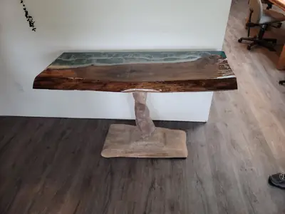 Live edge console table with a teal and grey epoxy river and a sculpted wood base against a white wall
