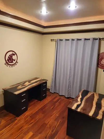 A dark office desk topped with a live edge epoxy slab, with a matching return, in a home office with wood floors.