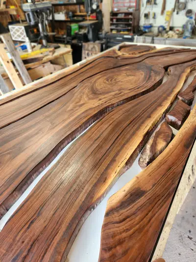 A live edge walnut kitchen counter running along a shop wall, its natural edge filled with a pale white epoxy river and finished to a high gloss.