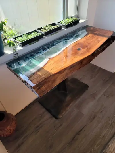 Narrow live edge table with a green epoxy river on a steel base set beneath a window