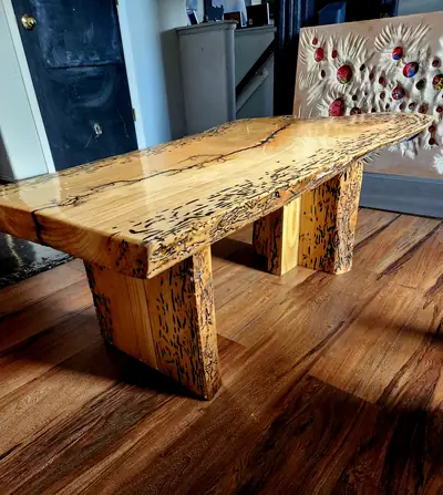 A spalted live edge dining table with heavy square legs and a glass smooth finish, on a wood floor beside a wall of art.