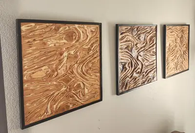 Three framed carved wood panels hung as a set, each cut in a different flowing grain pattern.