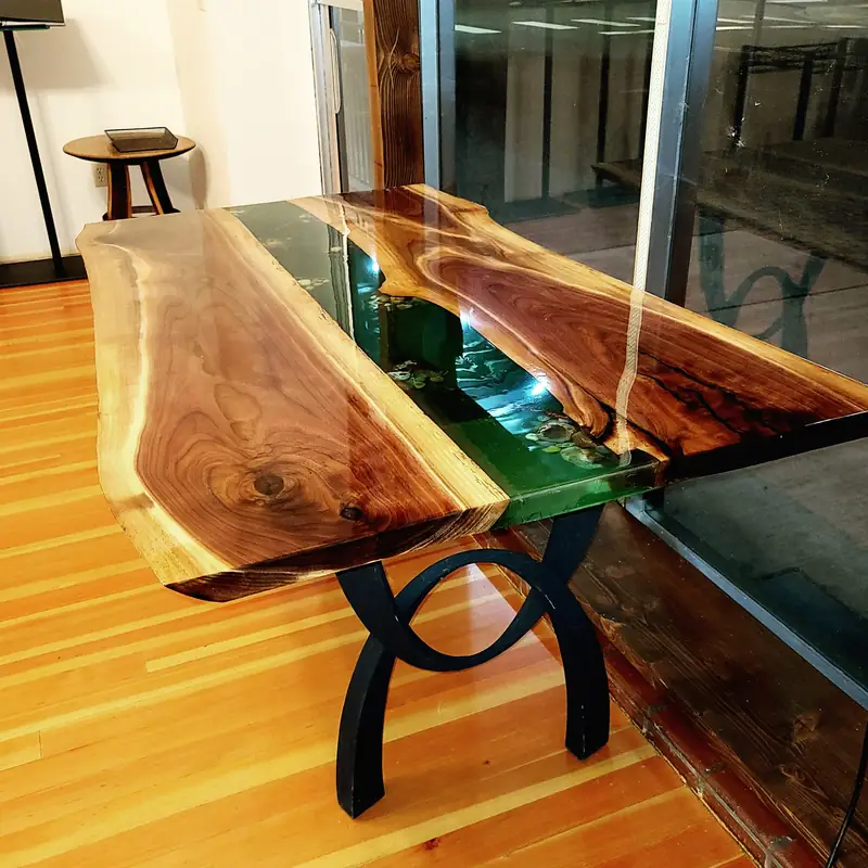 Live edge walnut river table with emerald green epoxy running through the centre, in a sunlit room
