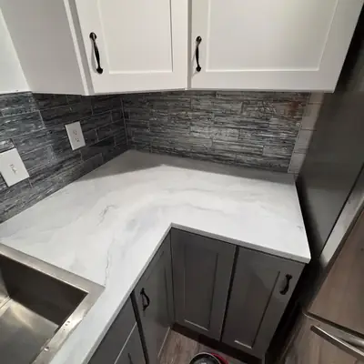 An L shaped run of white marble effect epoxy counters with grey veining, wrapping a corner under white upper cabinets.